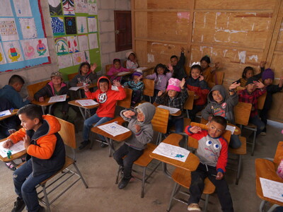 Kinder in Klassenzimmer winken zur Kamera