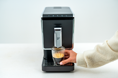 Hand nimmt Espresso unter Kaffeemaschine hervor