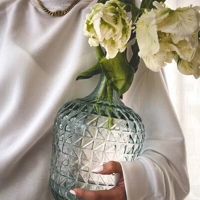 Hand hält gemusterte Glasvase mit weißen Blumen