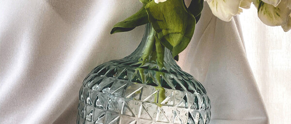 Hand hält Vase mit weißen Blumen vor hellem Stoff