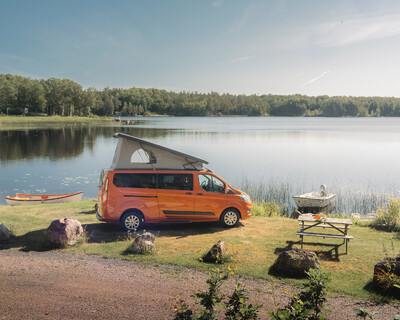 Orange Campervan am See mit Boot und Picknicktisch