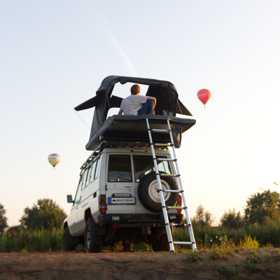 Mann im Dachzelt auf Jeep, Heißluftballons am Himmel