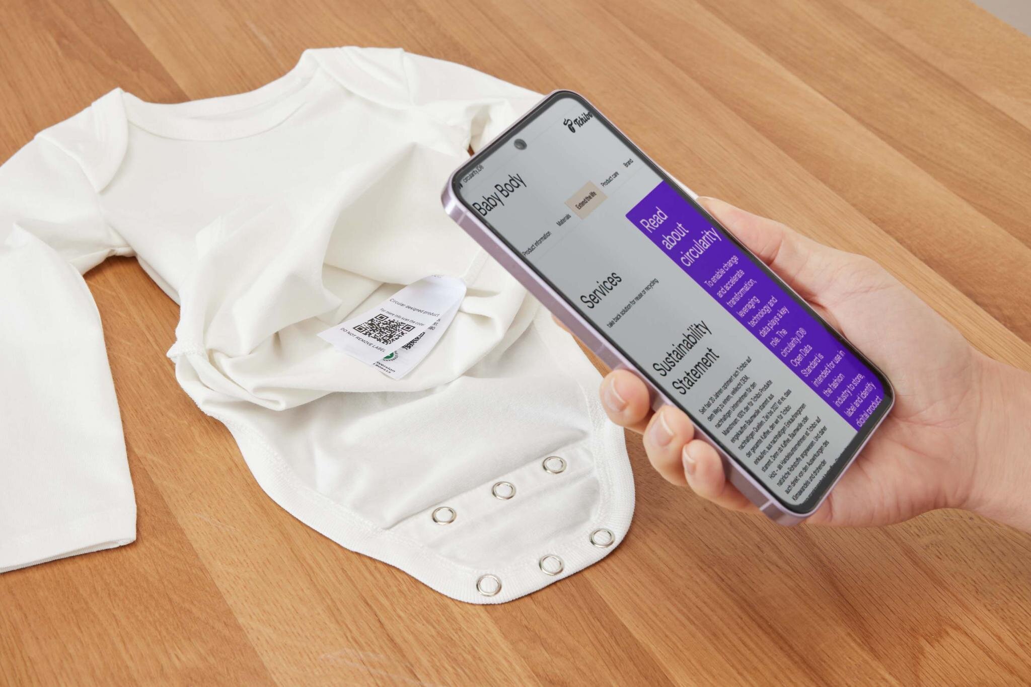 Hand scannt QR-Code an weißem Babybody mit Handy