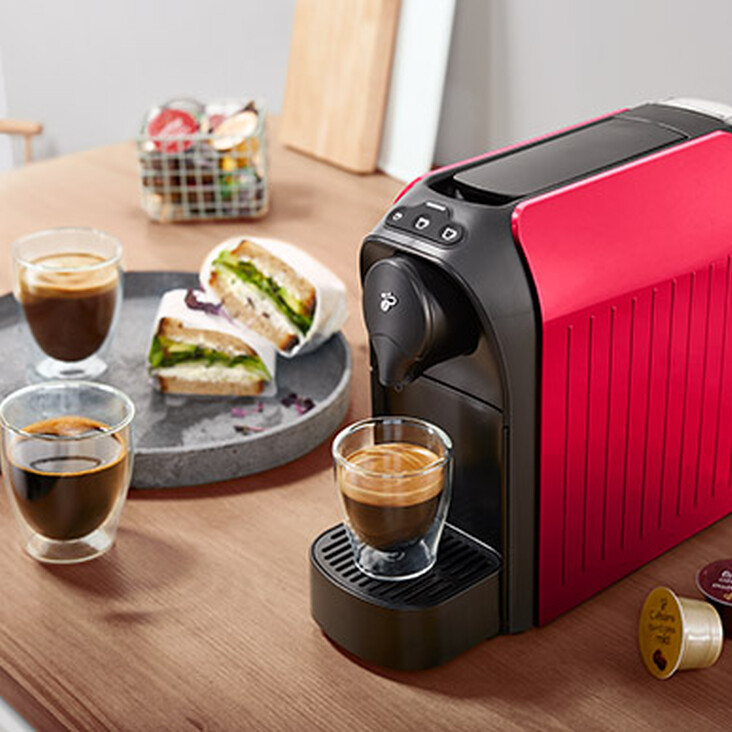 Rote Kapsel-Kaffeemaschine mit Espresso auf Holztheke