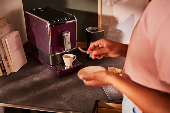 Person bereitet Kaffee an lila Maschine zu