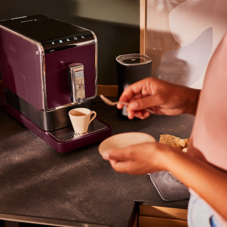 Person bereitet Kaffee an lila Maschine zu