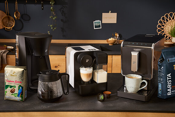 Drei Kaffeemaschinen mit Tassen und Kaffeepackungen
