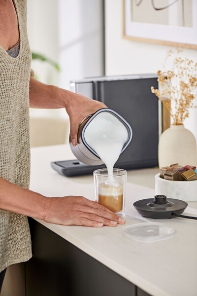Person gießt Milchschaum in ein Kaffeeglas