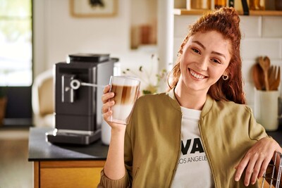Person hält Latte Macchiato vor Kaffeemaschine