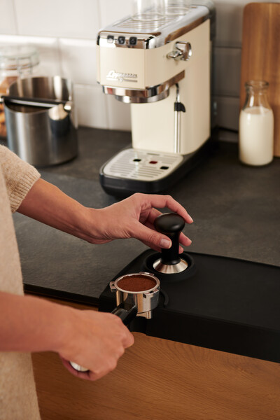 Hand tampert Espressopulver neben Maschine