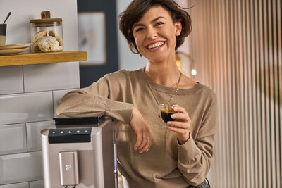 Person mit Espresso neben Kaffeemaschine