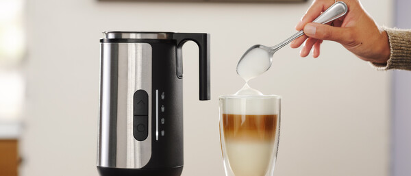 Hand löffelt Milchschaum in Latte Macchiato