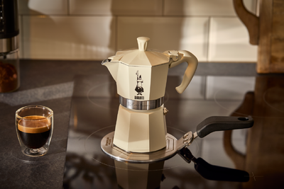 Cremefarbener Espressokocher auf Herd neben Tasse