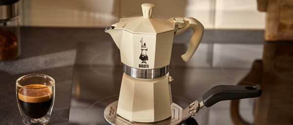 Cremefarbener Espressokocher auf Herd neben Tasse