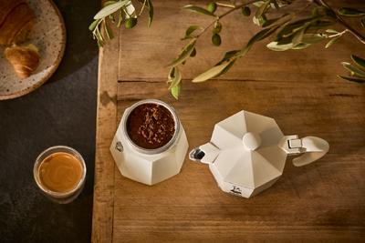 Espressokanne, Kaffeepulver, Glas Kaffee, Croissant