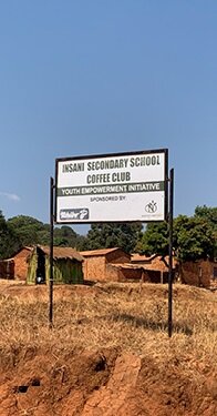 Schild der Insani Secondary School vor Lehmhäusern