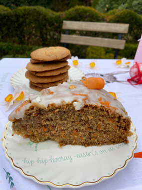 Karottenkuchen mit Glasur, dahinter Kekse auf Teller
