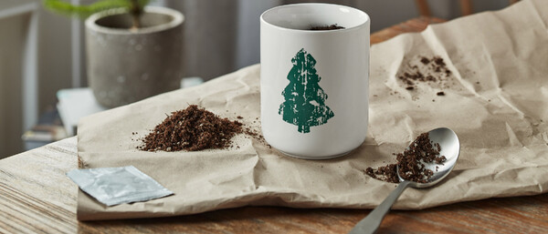 Becher mit Tannenbaum, Erde und Löffel auf Papier