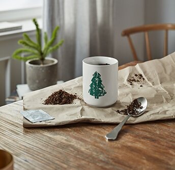 Tasse mit Tannenbaum, Erde und Löffel auf Papier
