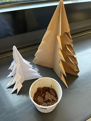 Papier-Tannenbäume neben Becher mit Erde