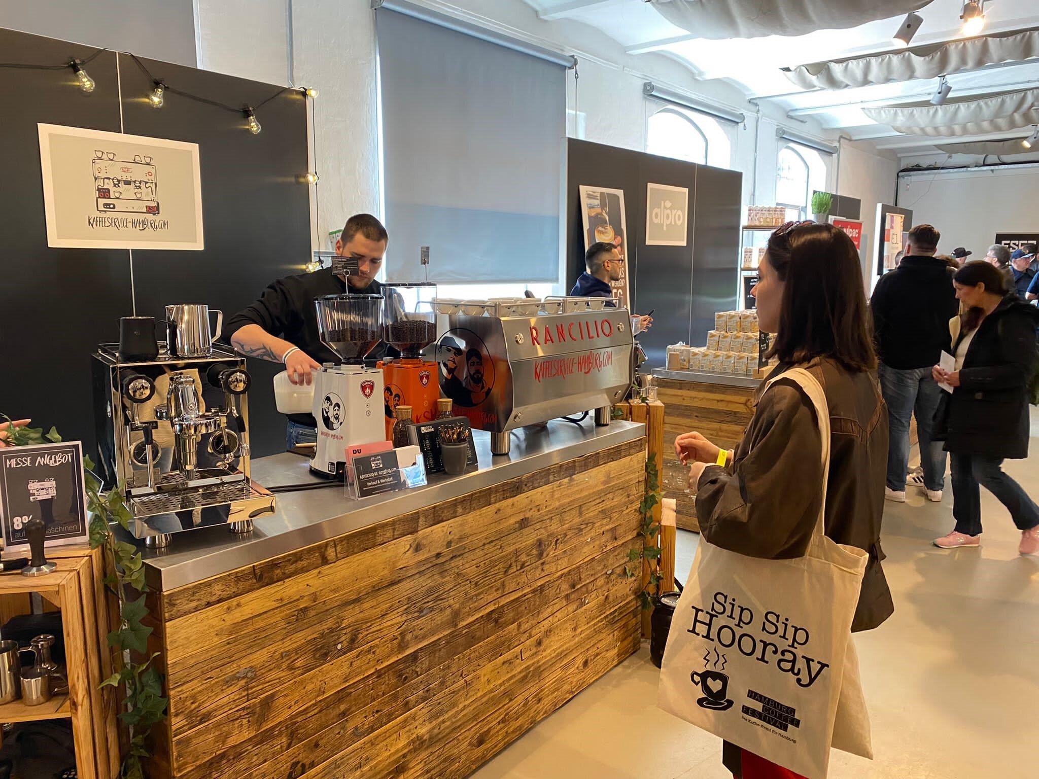 Frau mit Stoffbeutel bestellt Kaffee am Messestand