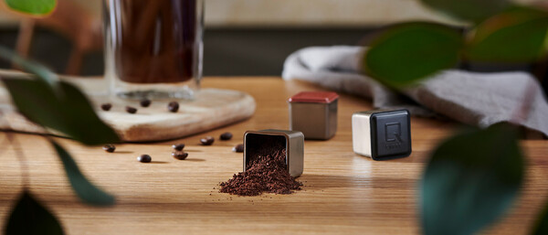 Kaffee­pulver und Bohnen neben Metallkapseln