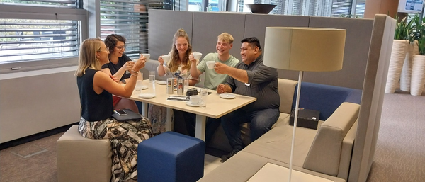 Fünf Kollegen stoßen mit Kaffeetassen im Büro an