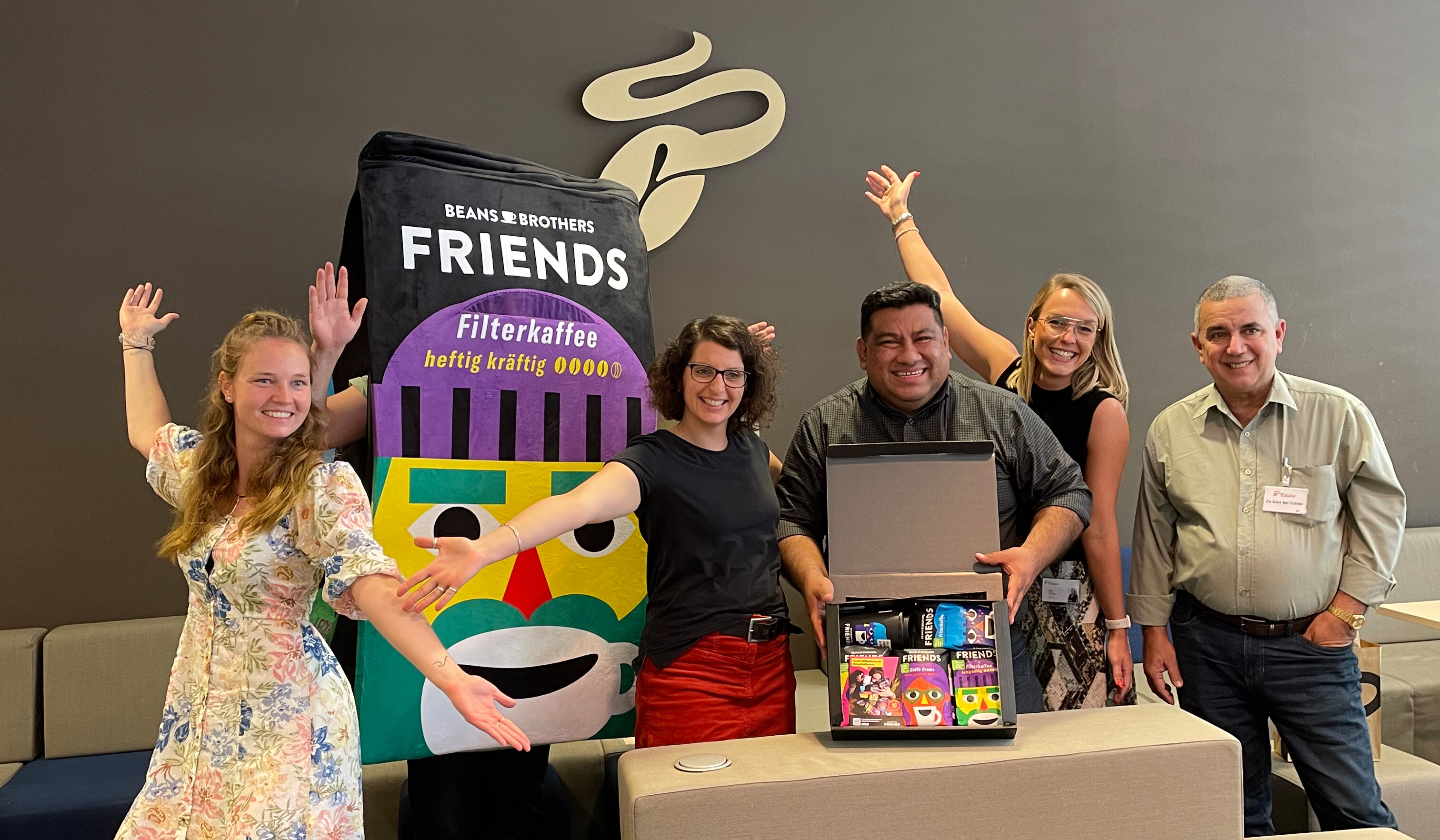 Gruppe posiert mit riesiger Kaffeepackung und Geschenkbox