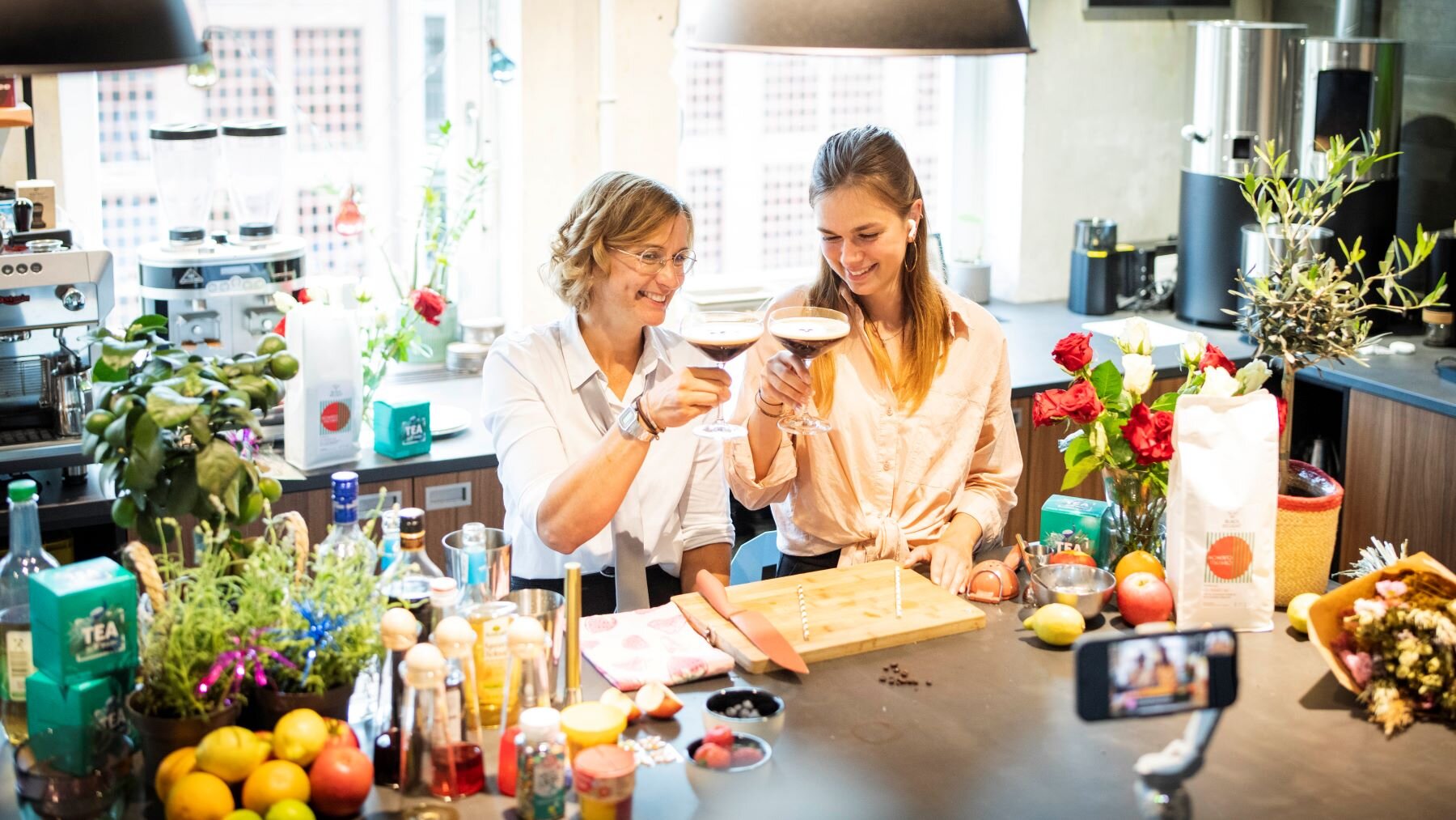 Zwei Frauen stoßen in heller Küche mit Cocktails an