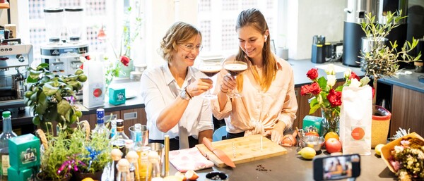 Zwei Frauen stoßen in heller Küche mit Cocktails an