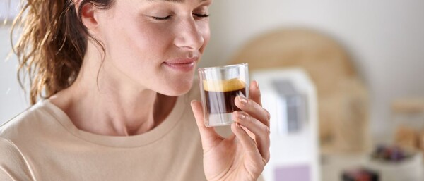 Person hält Glas Espresso vor Kaffeemaschine