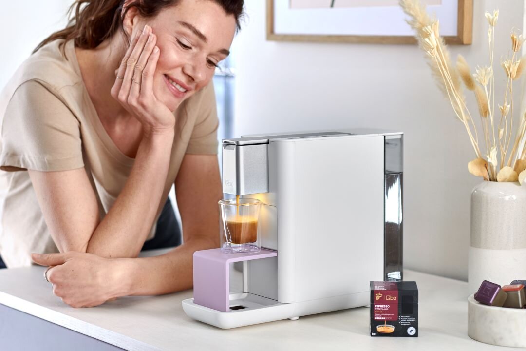 Frau lächelt neben moderner Kaffeekapselmaschine