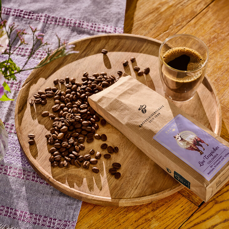 Kaffeebohnen, Kaffeetasse und Blumen auf Holzteller