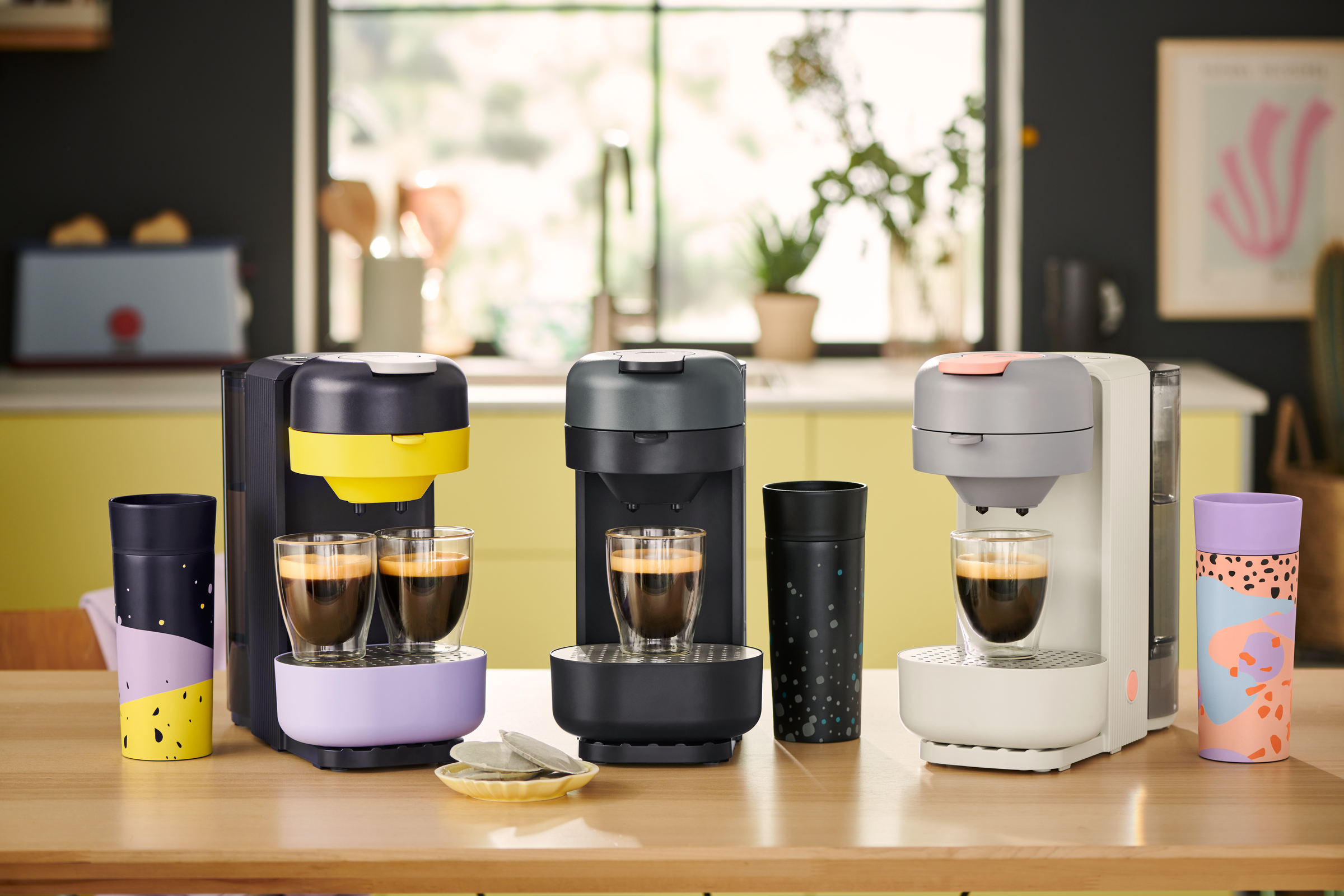 Drei bunte Kaffeepadmaschinen mit Bechern