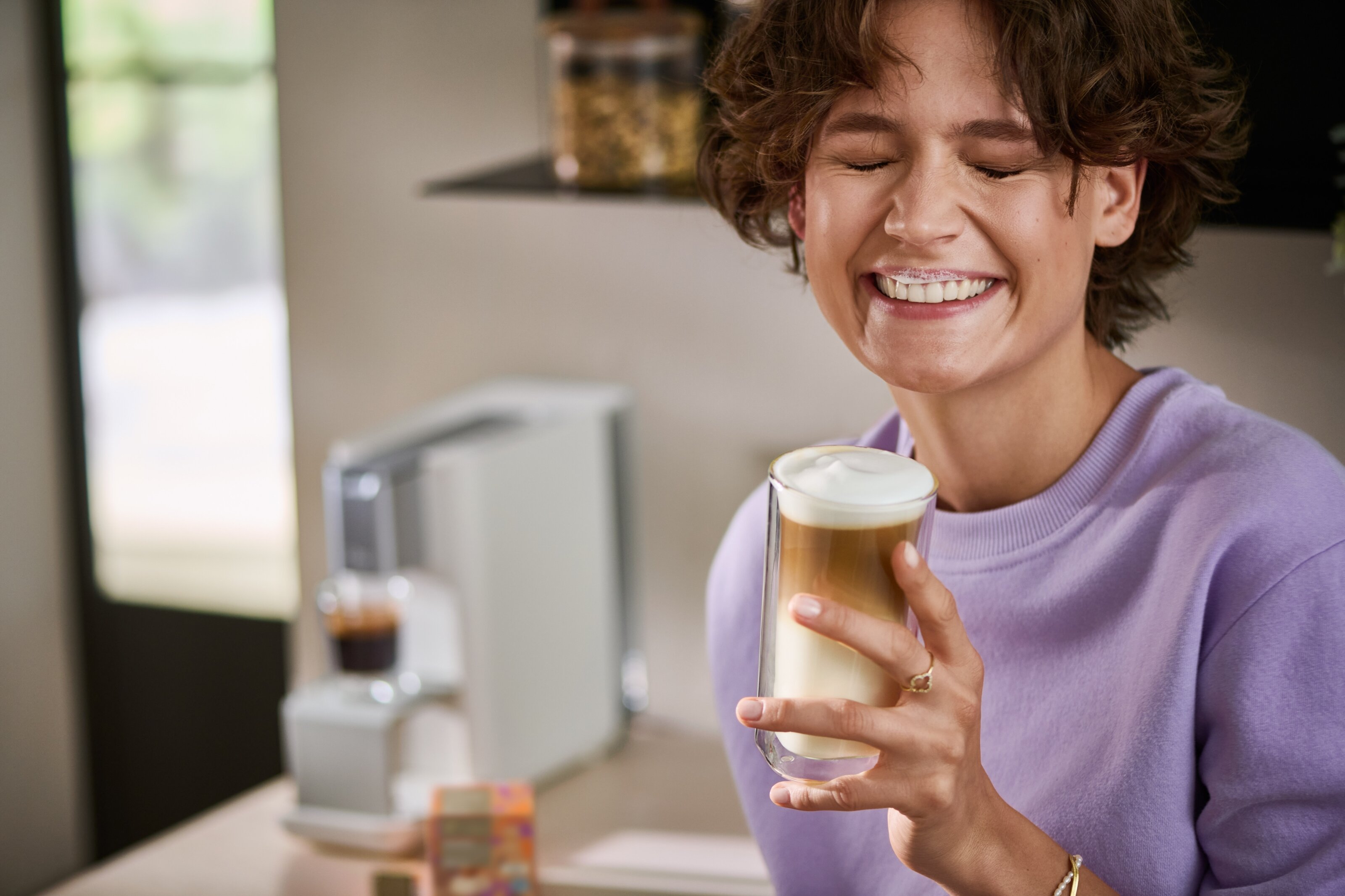 Person hält Latte Macchiato neben Kaffeemaschine