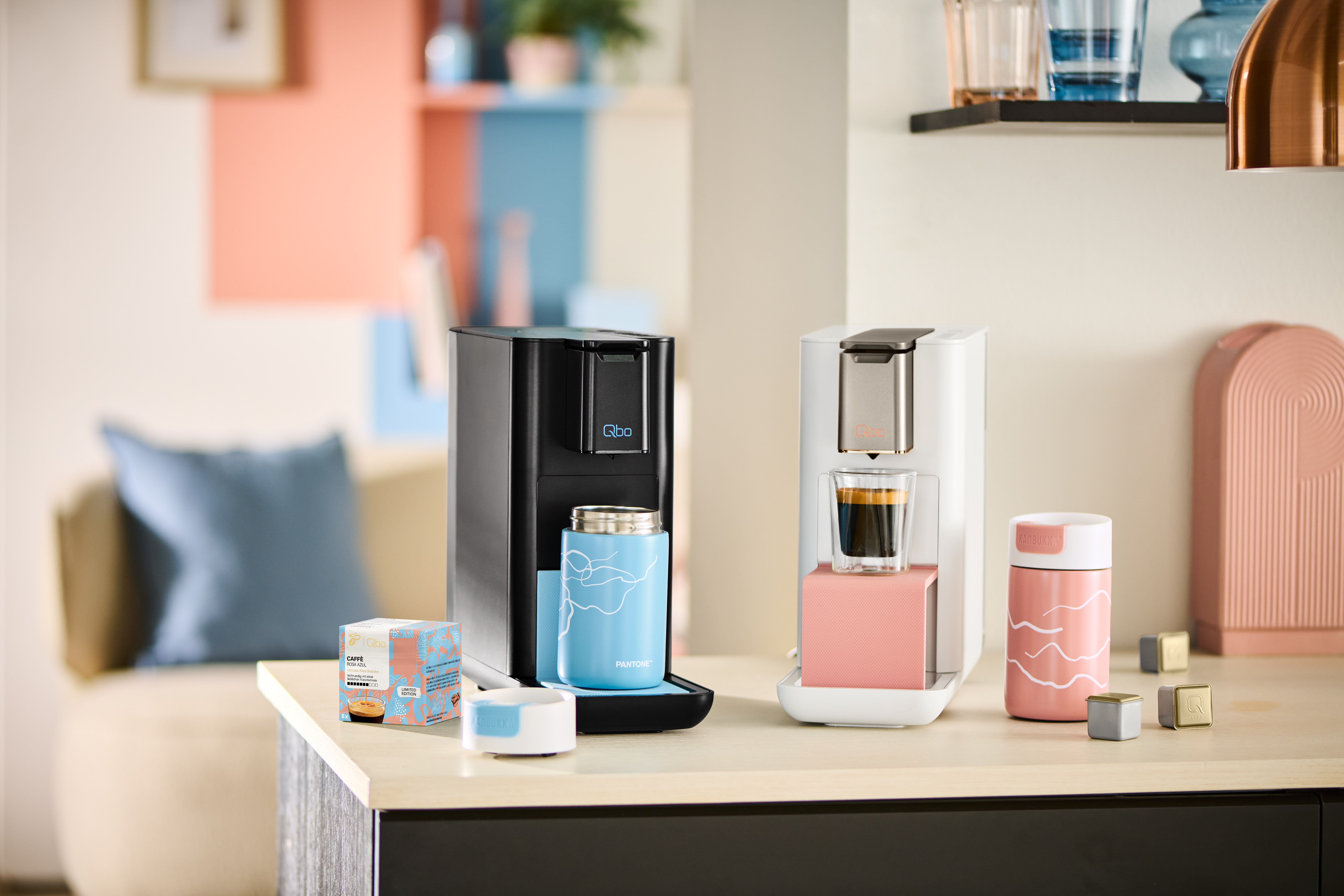 Zwei Qbo-Kaffeemaschinen mit Bechern auf Küchenzeile