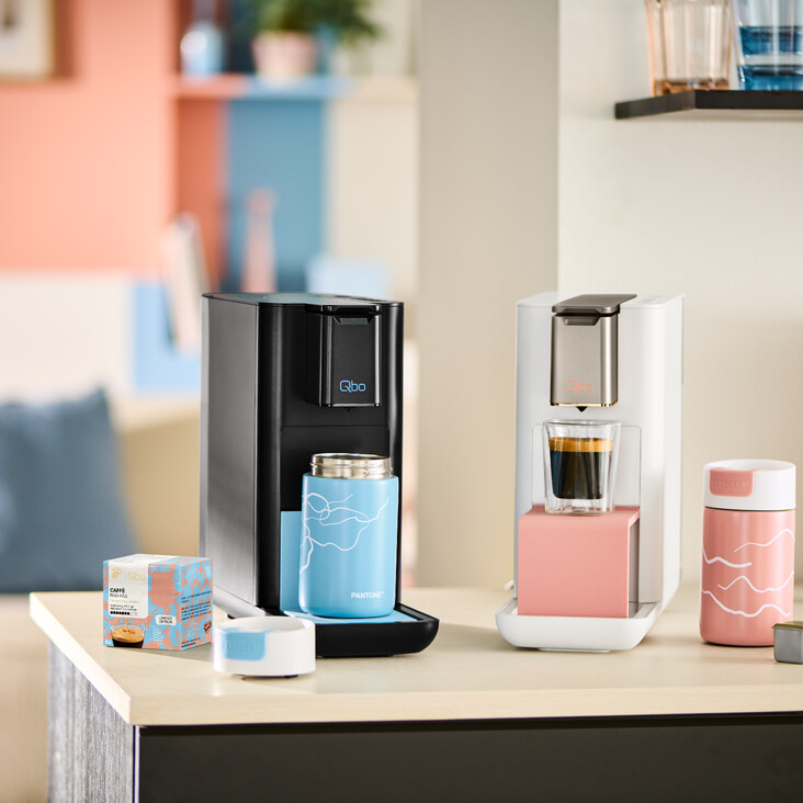 Zwei Qbo-Kaffeemaschinen mit Bechern auf Küchenzeile