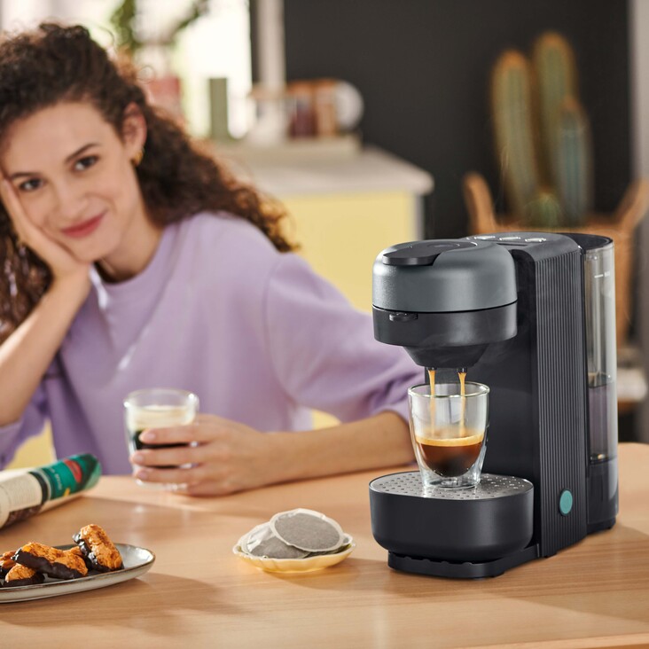 Frau trinkt Kaffee neben moderner Kaffeemaschine