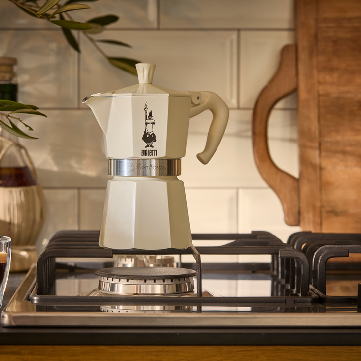 Cremefarbene Espressokanne auf Gasherd, Glas Kaffee