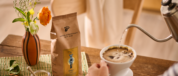 Hand brüht Kaffee neben Kaffeepackung und Blume