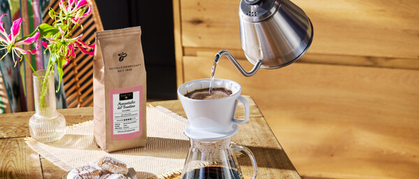 Hand gießt Filterkaffee, Bohnen, Gebäck daneben