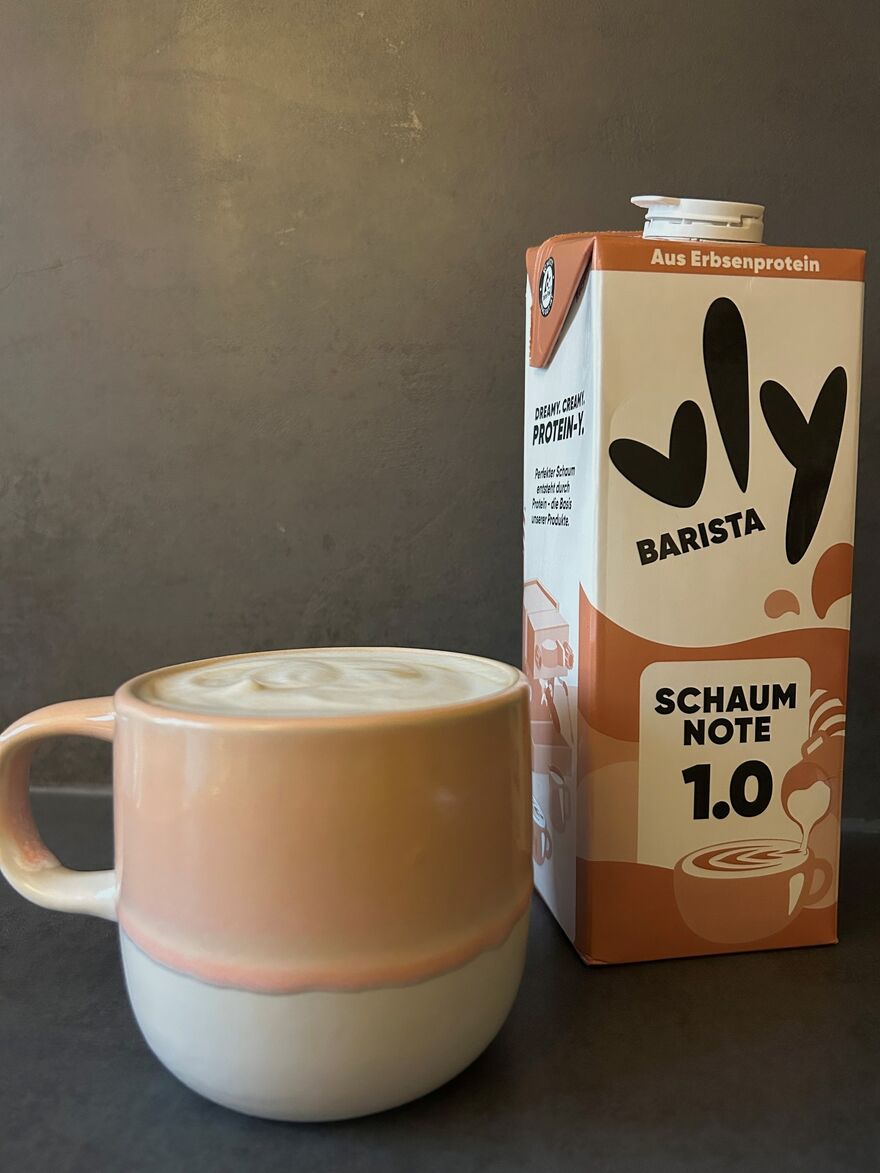 Latte in Tasse neben vly Barista Hafermilchkarton