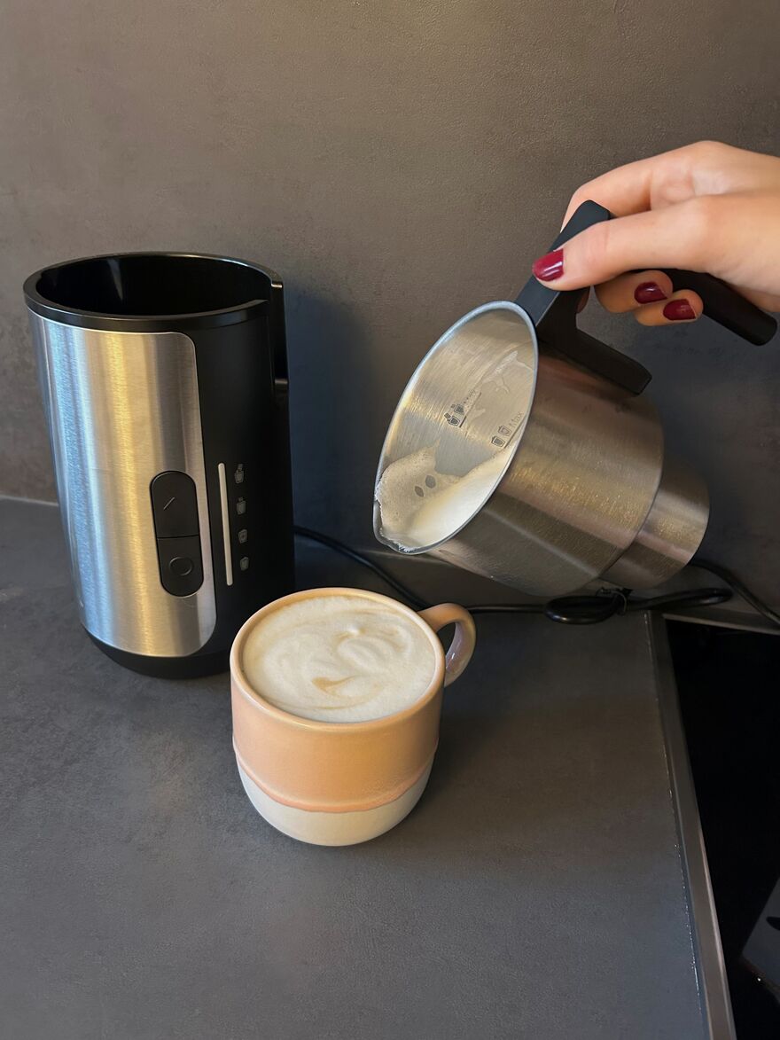 Hand schäumt Milch in beige Tasse Latte Macchiato