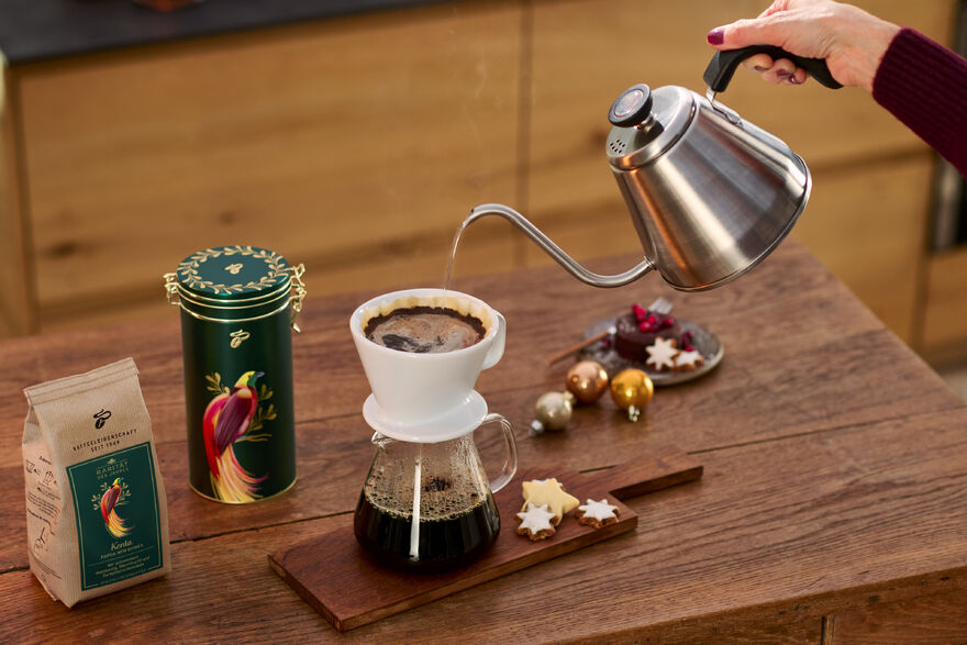 Hand gießt Filterkaffee, Kekse und Deko auf Tisch