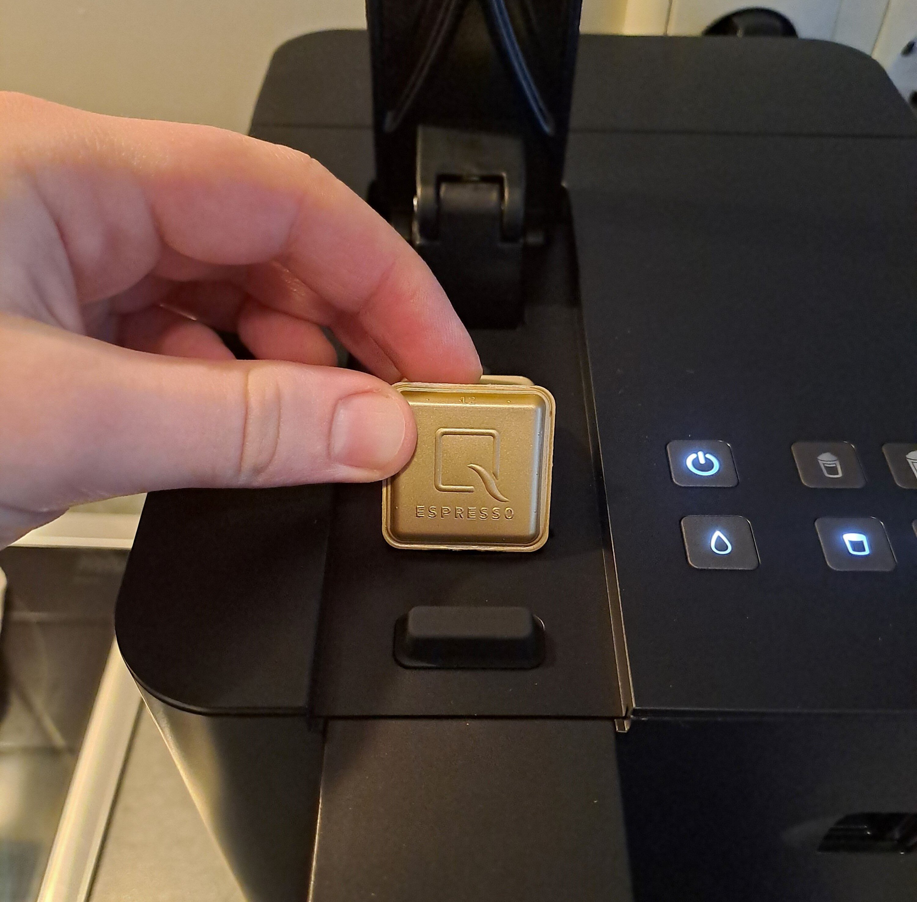 Hand setzt goldene Espressokapsel in Kaffeemaschine
