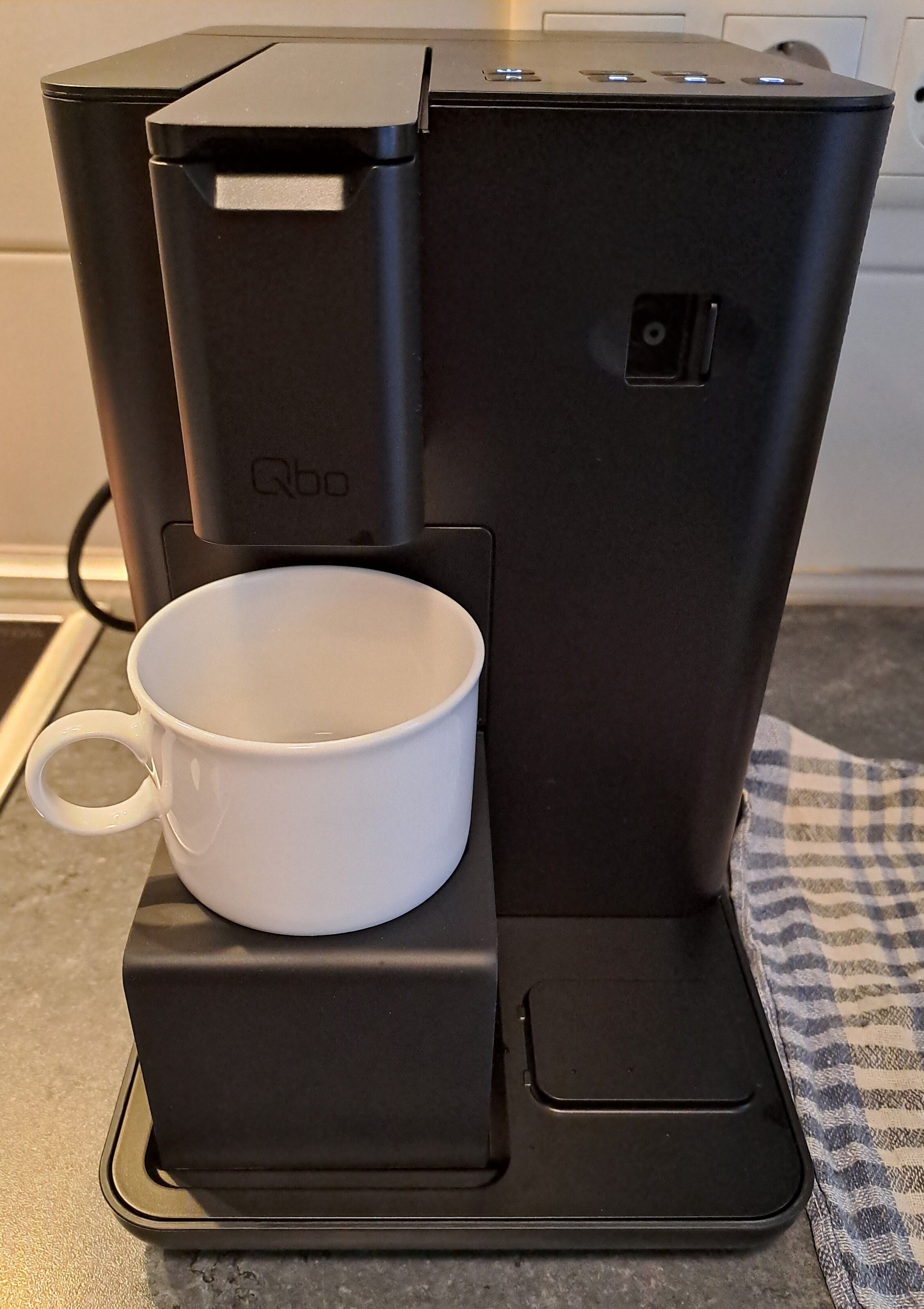 Schwarze Qbo-Kaffeemaschine mit leerer weißer Tasse