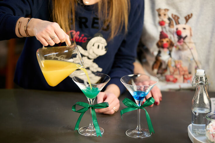 Hand gießt Saft in bunte Cocktails im Glas