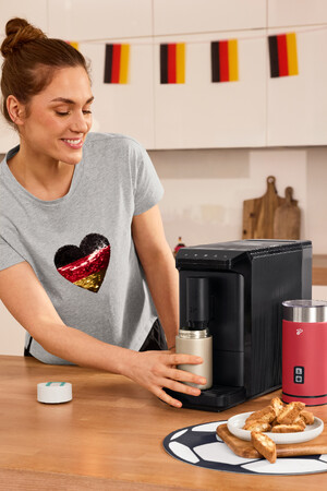 Link: Großansicht des Bildes - Bildinhalt: Frau bedient Kaffeemaschine, deutsche Deko im Hintergrund