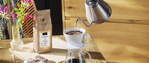 Hand gießt Kaffee in Filter, Bohnen und Gebäck nearby