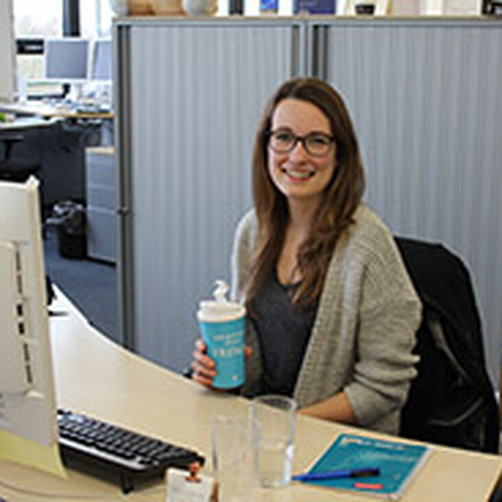 Frau am Schreibtisch mit Computer und Getränk